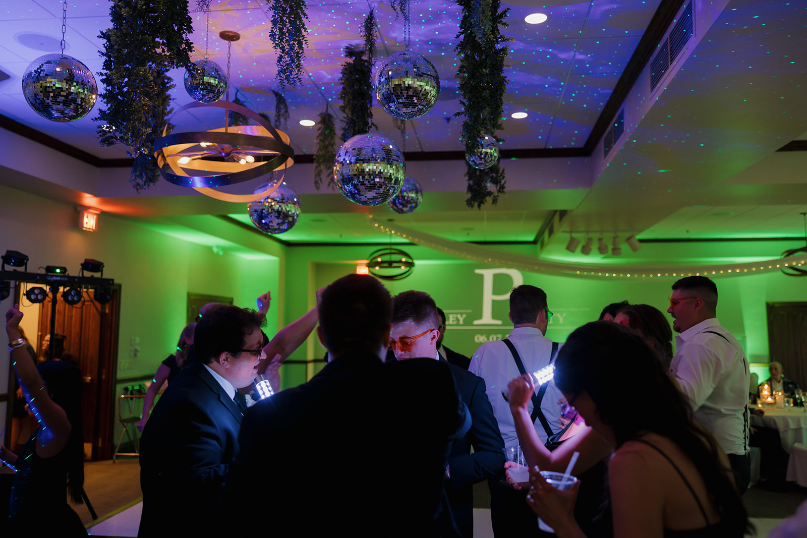 Guests dancing under moody green lights and glittering disco balls during the evening celebration at a country club wedding reception.