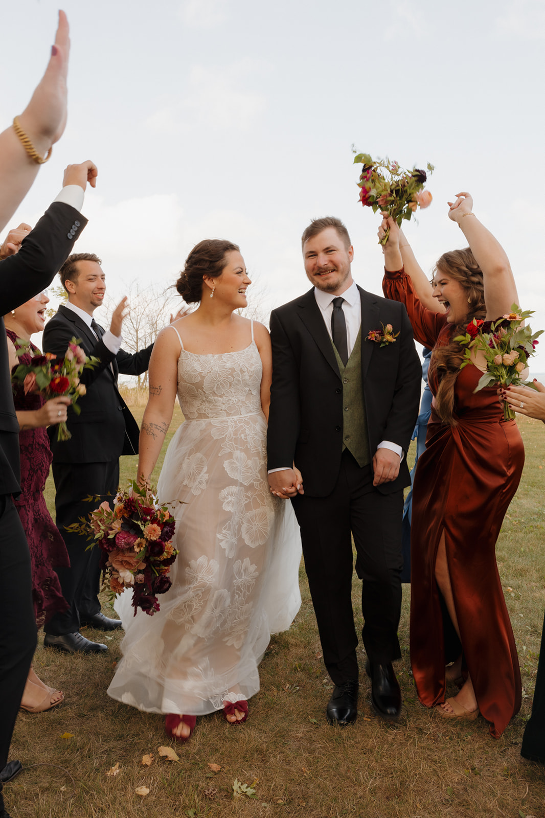 Bride and groom walk hand-in-hand through cheering bridal party with bold fall florals and big smiles during their Wisconsin wedding celebration.