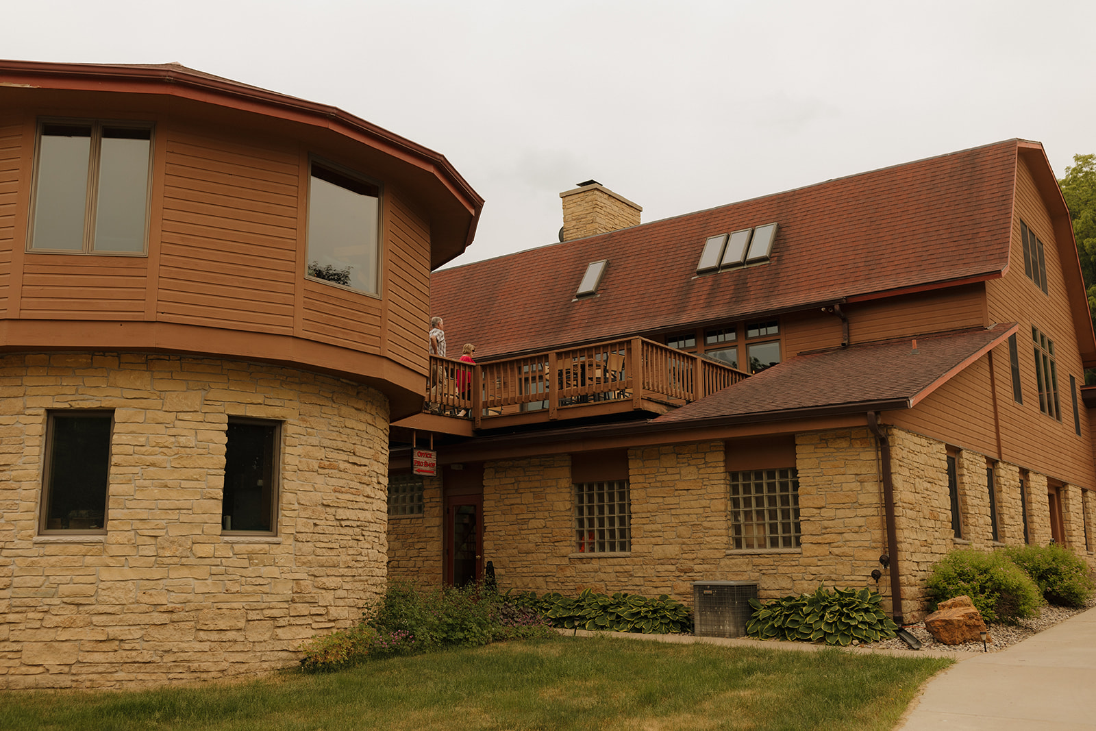 Exterior view of a rustic lodge-style venue with stone and wood architecture, where guests gather on the upper balcony before the celebration begins.