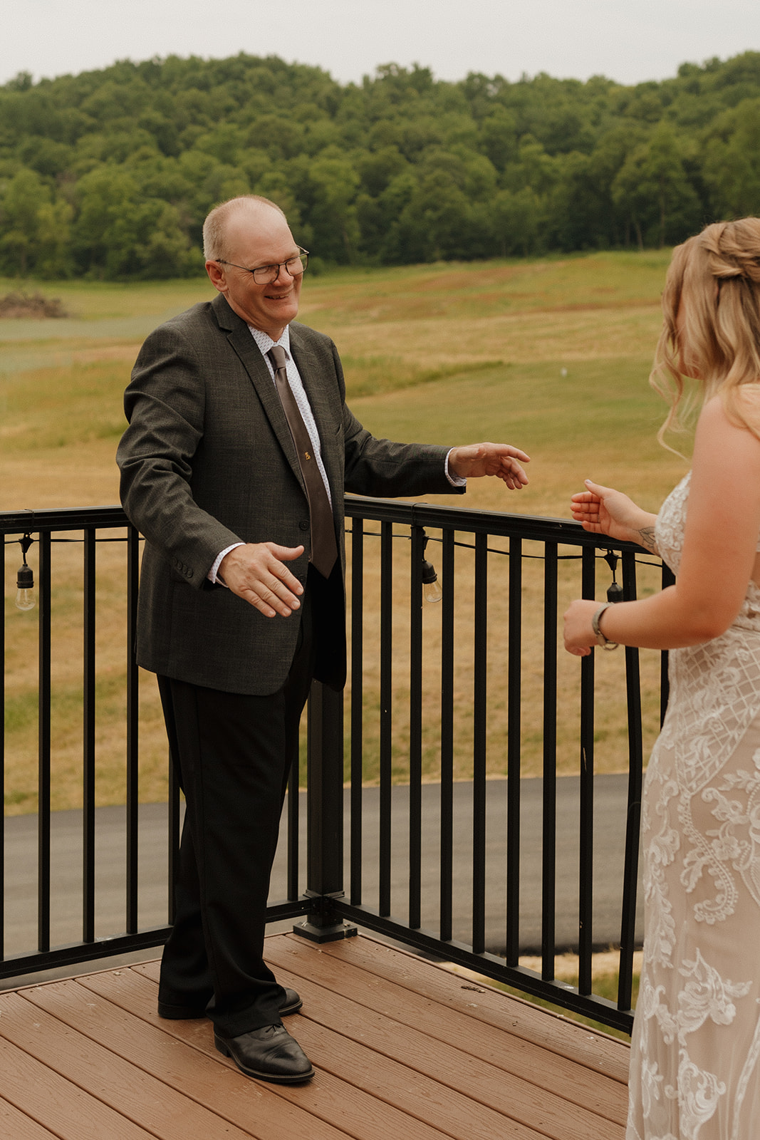 Bride and father see each other for the first time before the ceremony, arms open and eyes welling up on a balcony overlooking lush fields.