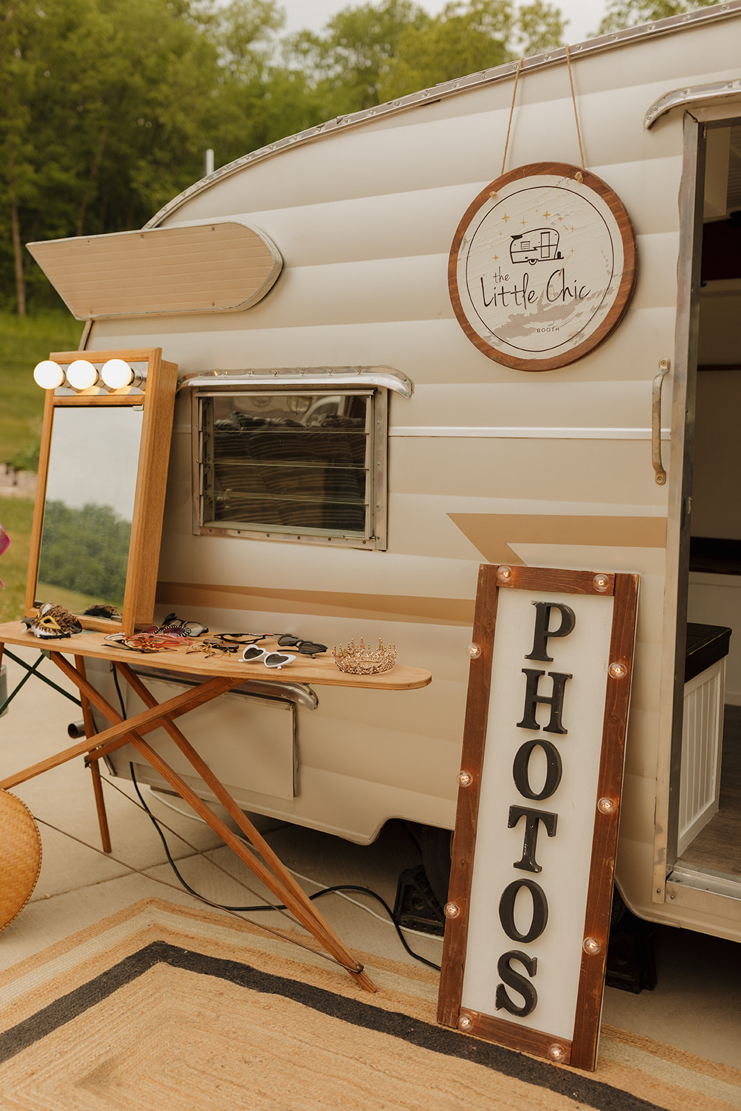 A vintage camper turned photo booth, complete with vanity mirror, props, and a lit-up "PHOTOS" sign, ready for guests to snap fun memories.