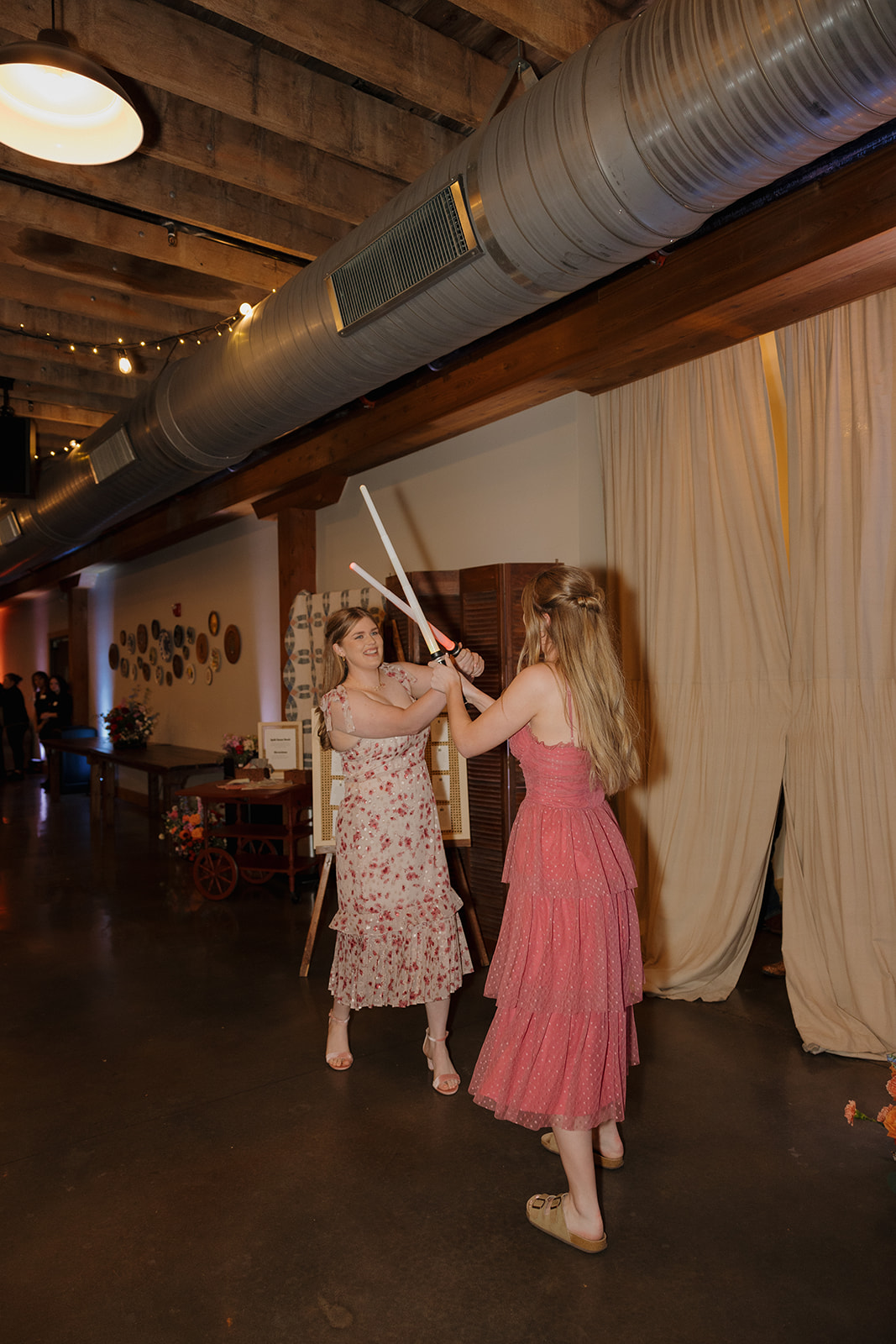 Bridesmaids bring a bit of whimsy to the reception with a playful lightsaber duel in the barn venue hallway.