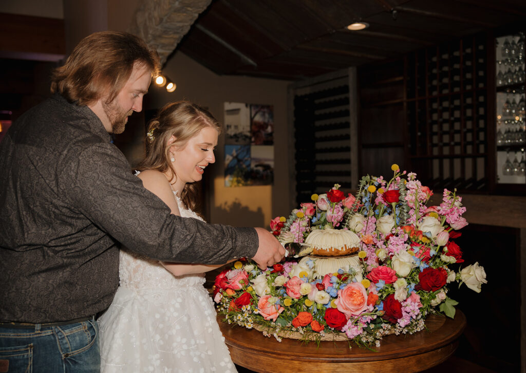 The newlyweds cut their bundt wedding cake framed with bright florals at their Wisconsin barn wedding.