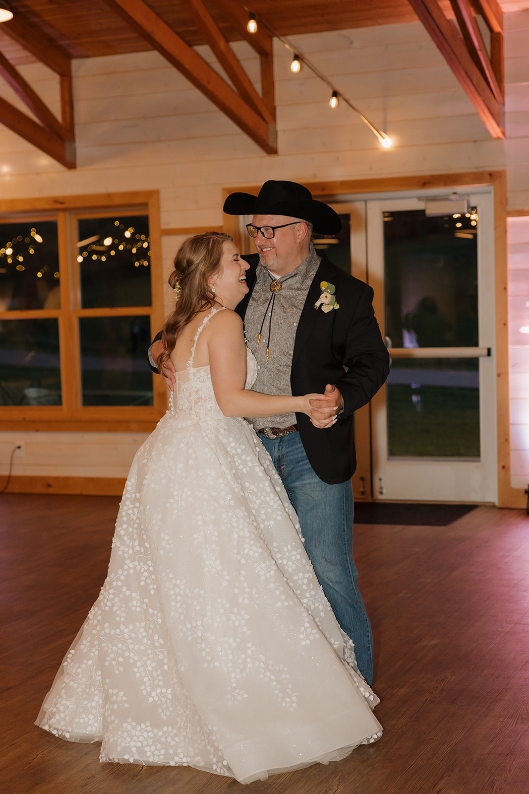 The bride smiles while sharing a joyful father-daughter dance at her barn wedding reception.