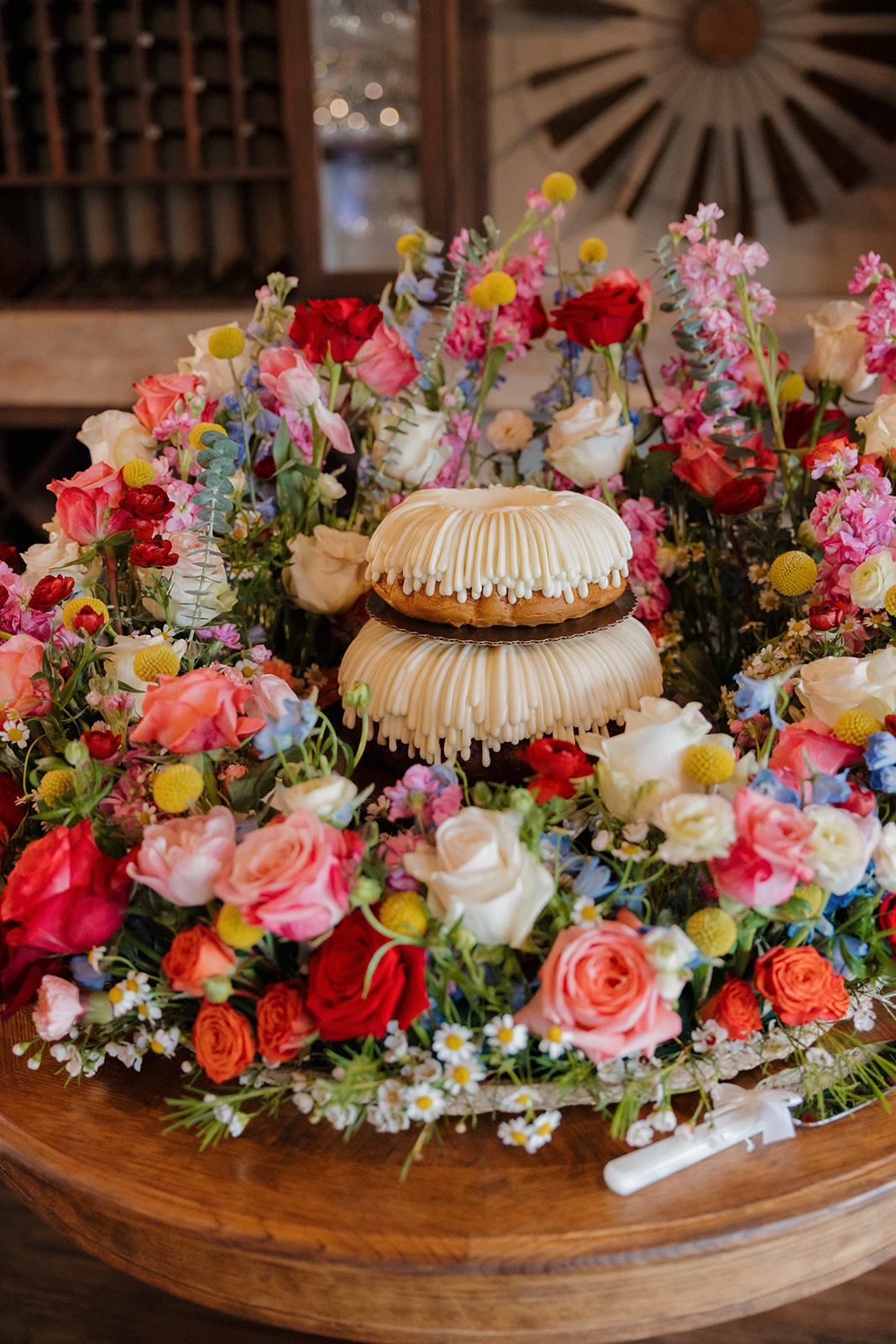 A tiered bundt cake surrounded by a vibrant wreath of spring flowers—playful dessert styling at a colorful Wisconsin barn wedding.