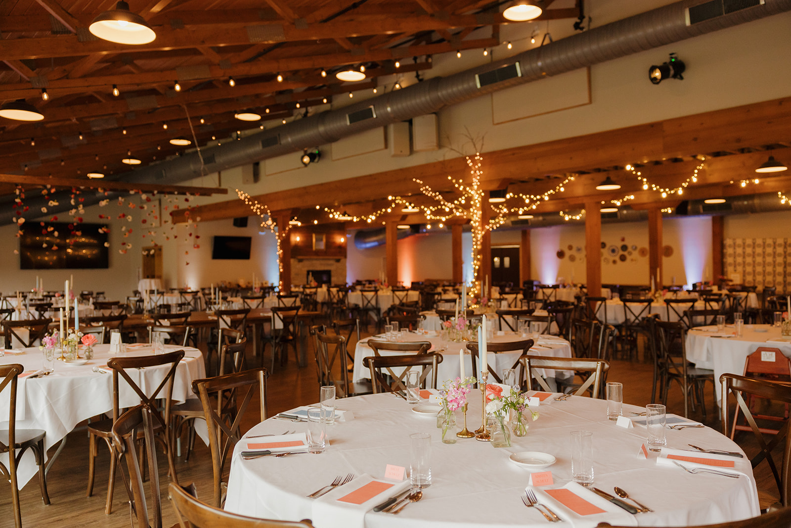 Reception hall decorated with soft lighting, florals, and round tables for a cozy Wisconsin barn wedding dinner.