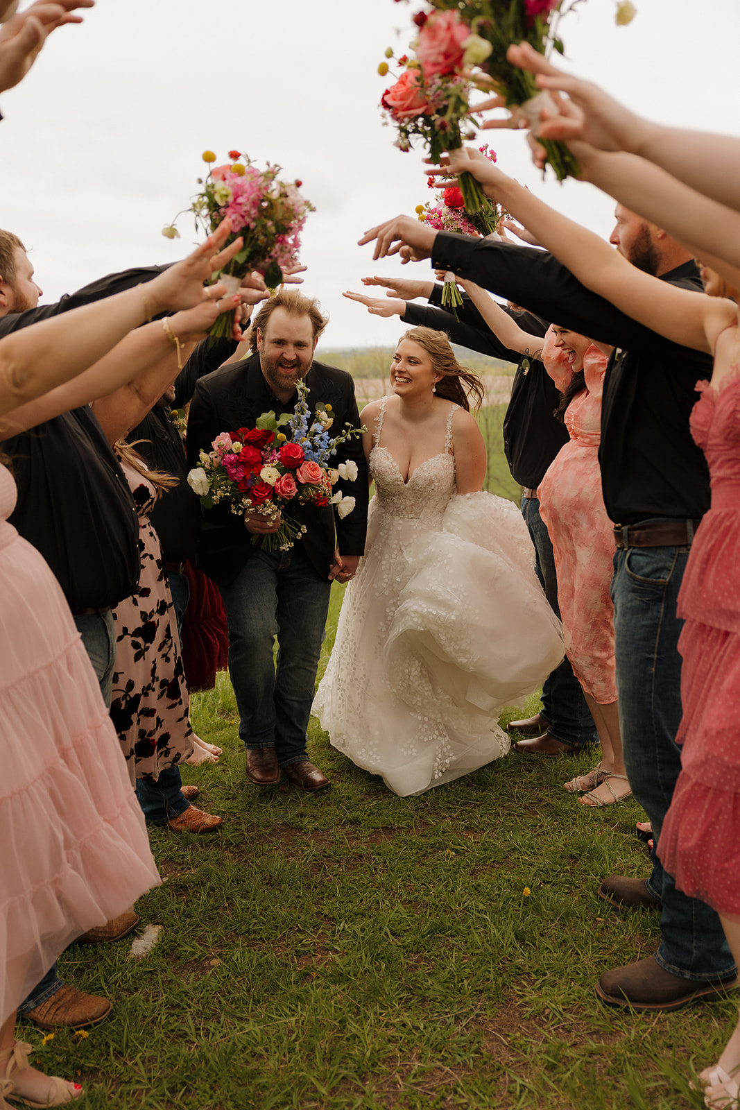 Bride and groom running through a tunnel of guests holding flower bouquets—full of movement, joy, and celebration at Vennebu Hill.