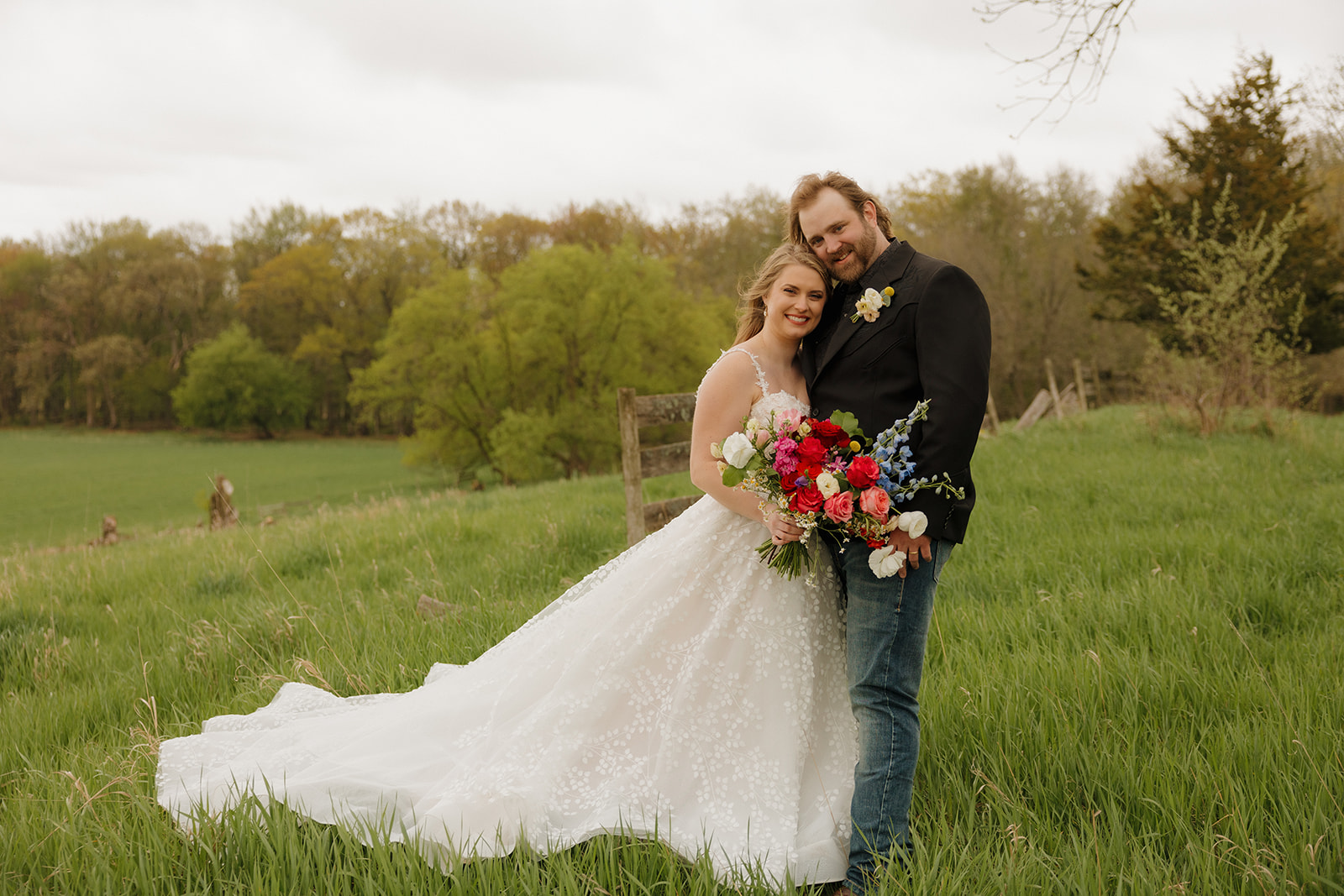 The couple pose together in a green pasture, celebrating their Wisconsin barn wedding with colorful spring florals.