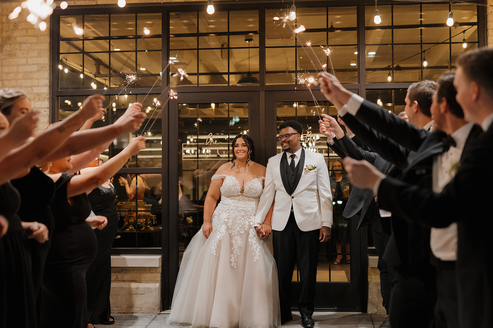 Bride and groom smiling during sparkler exit surrounded by cheering guests at their Milwaukee wedding reception.
