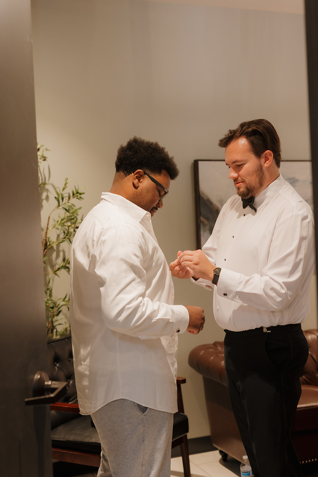 Groomsman helping the groom with cufflinks while getting ready on wedding day.
