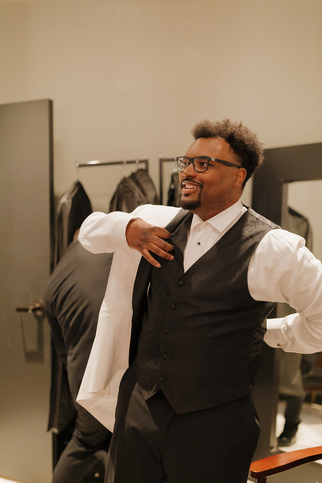 Groom smiling while getting dressed in a white tux jacket before his wedding ceremony.