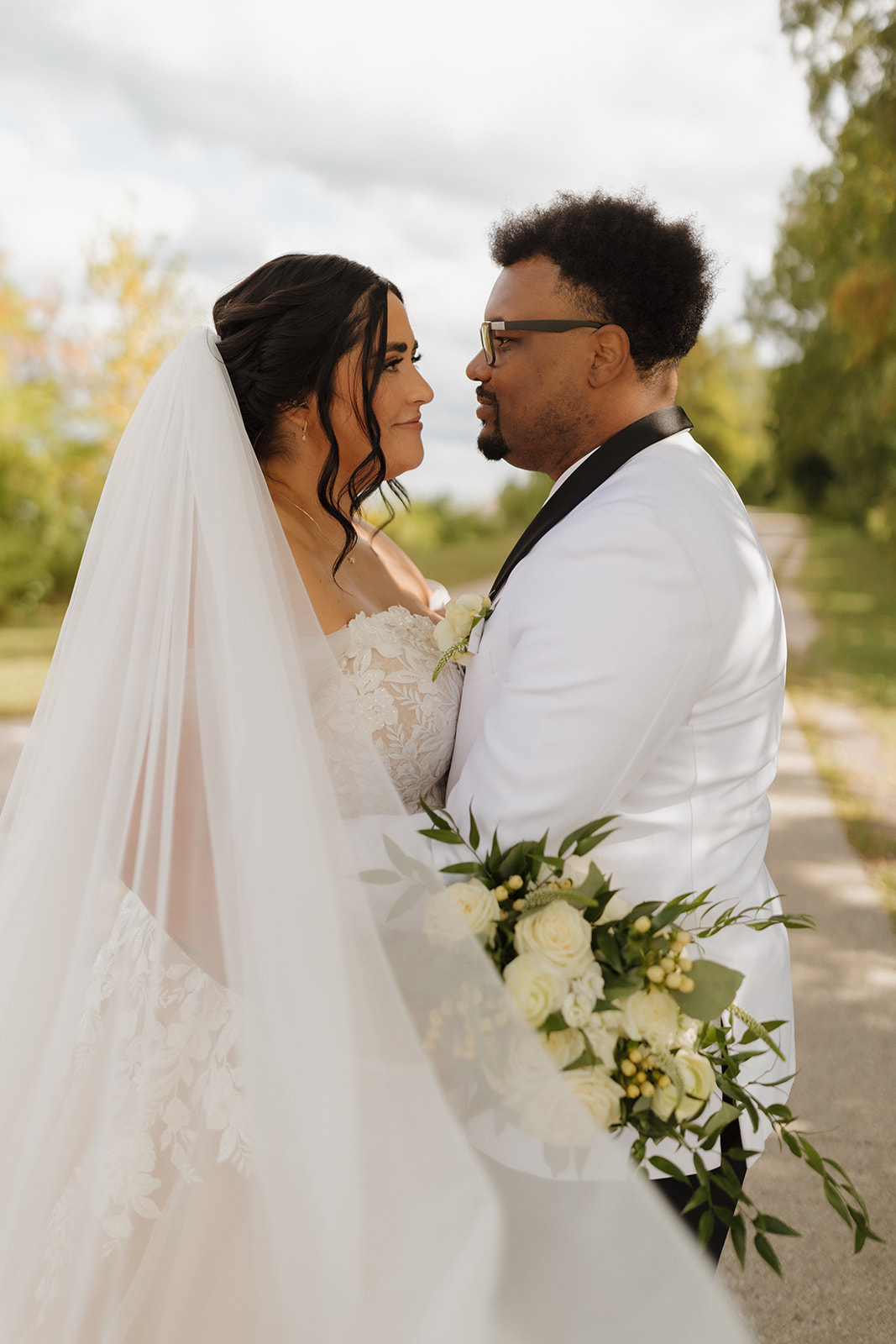 Groom holds bouquet while looking at his bride during a sunlit moment in South Shore Park.