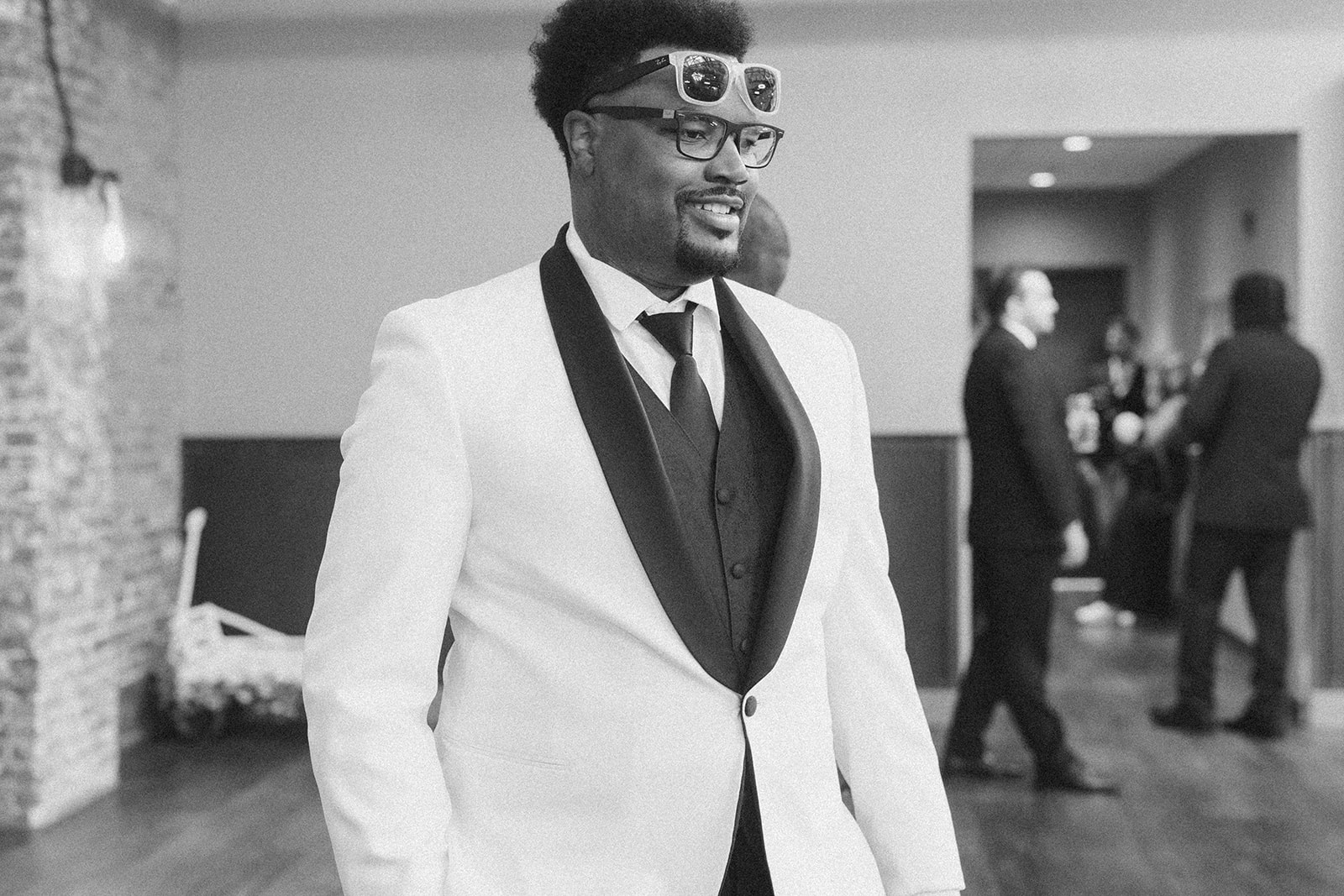 Groom in white tux and playful sunglasses surrounded by groomsmen at a Milwaukee wedding.