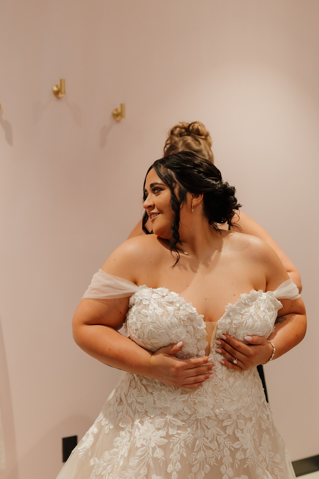 Bride smiling as she gets ready, adjusting the top of her floral lace wedding dress.