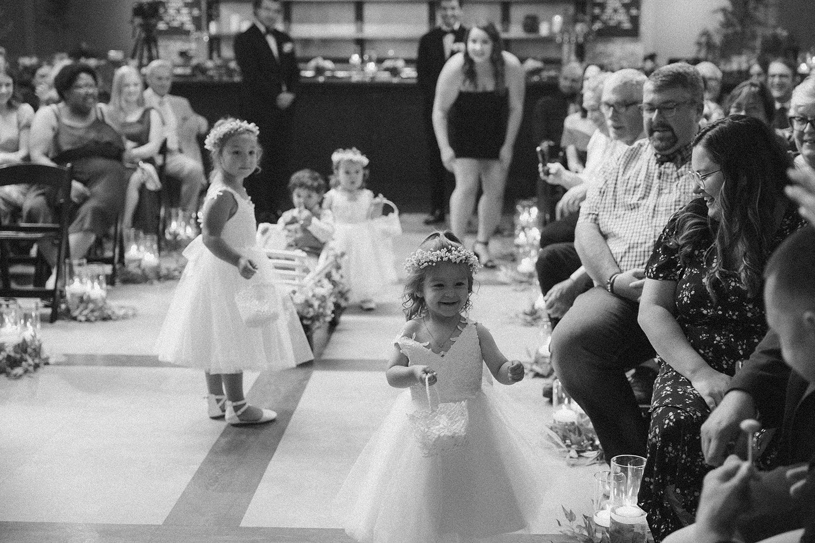 Young flower girls walk down the aisle at a Milwaukee wedding ceremony, smiling and scattering petals.