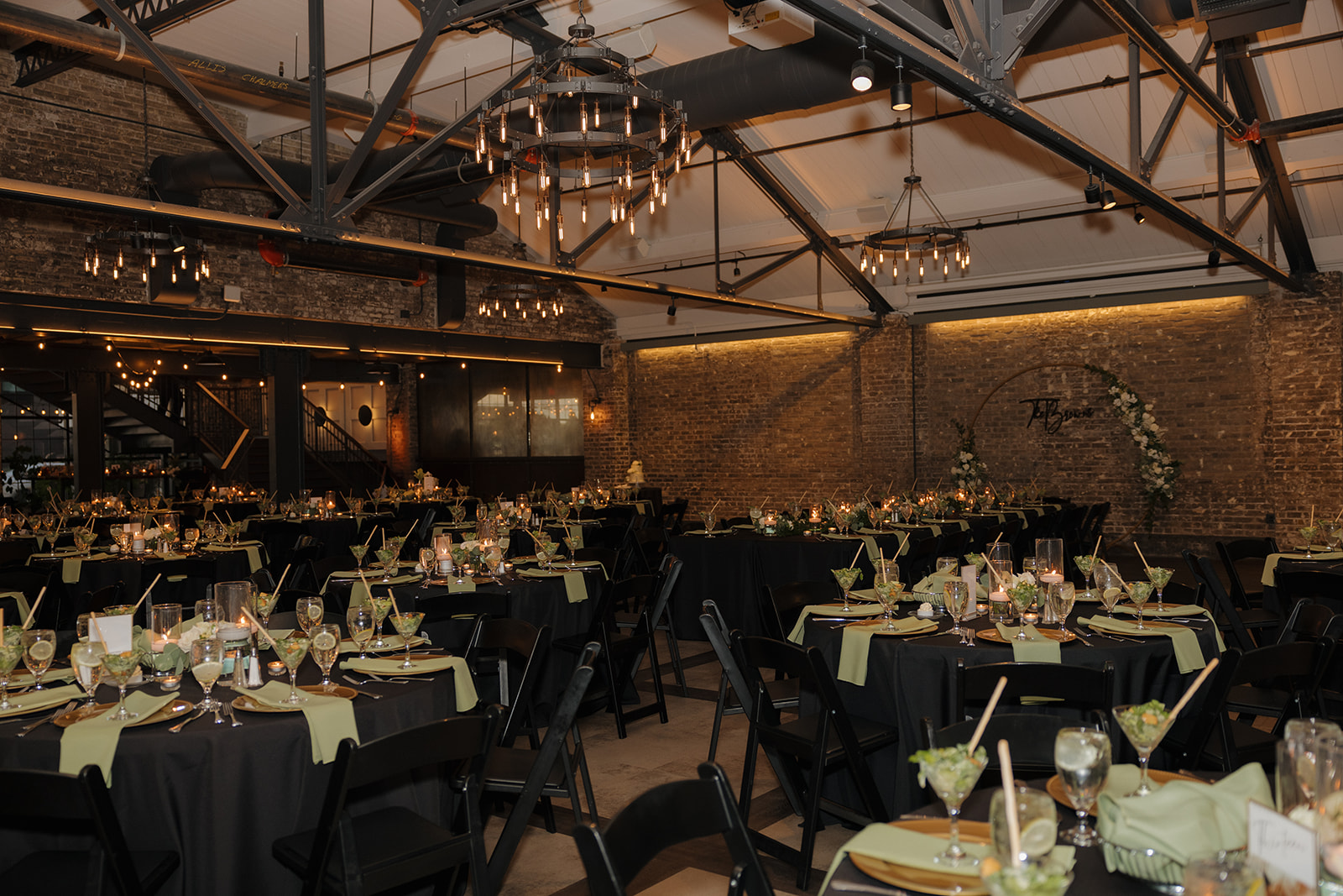 Industrial chic wedding reception setup with black chairs, sage napkins, and soft candlelight in a Milwaukee wedding venue.