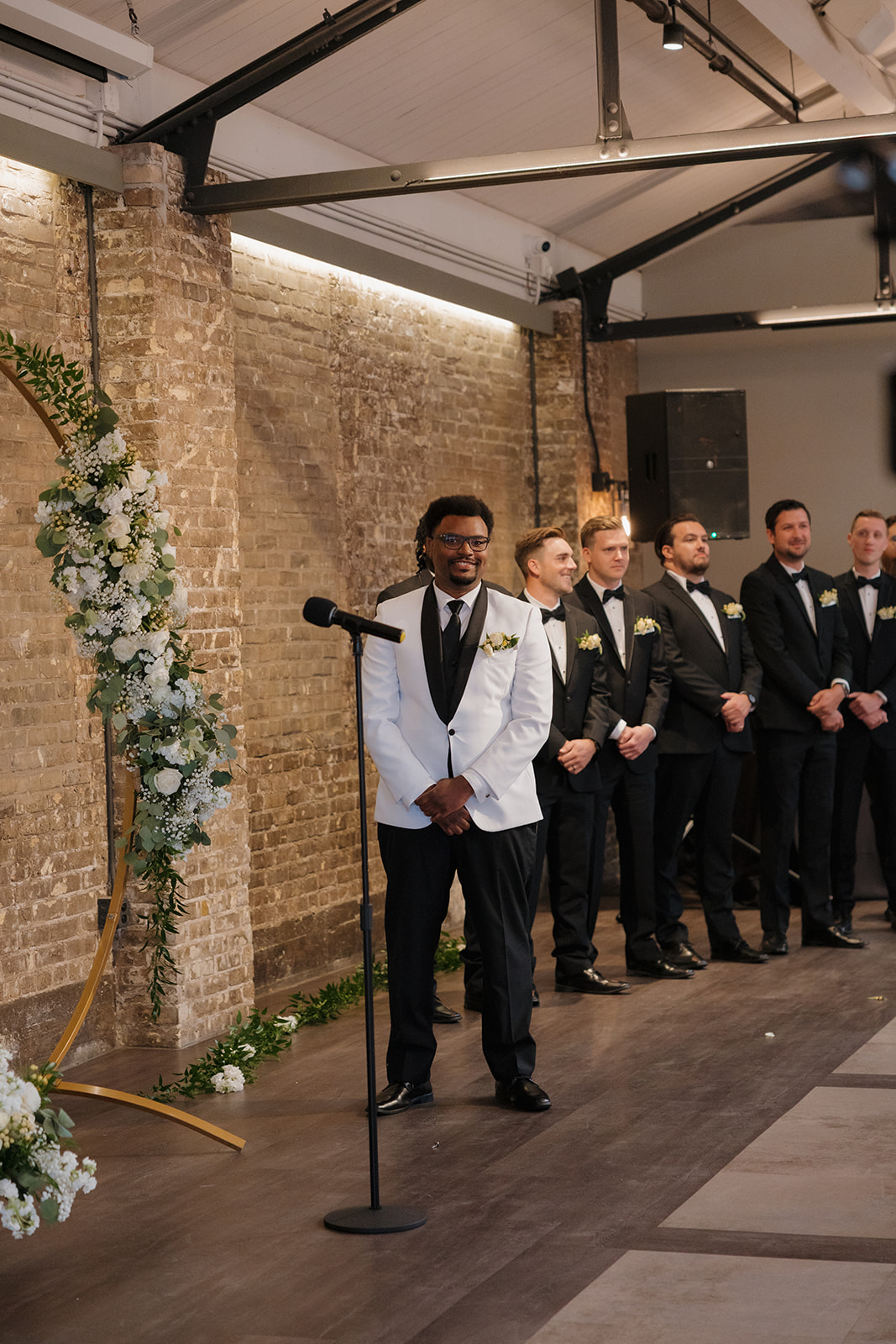 Groom stands at the altar in front of a floral arch, waiting for his bride at their Milwaukee wedding.