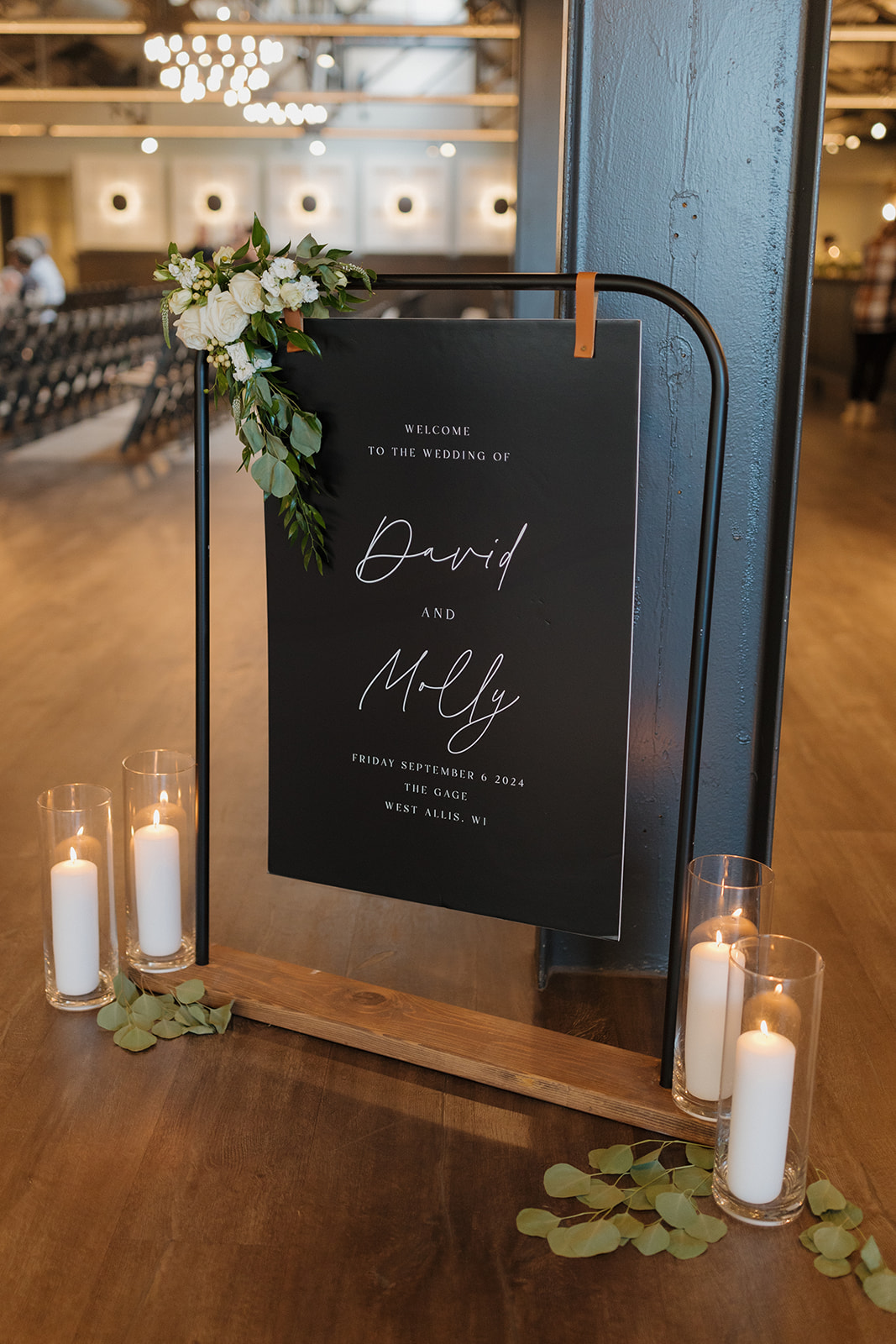 Elegant black wedding welcome sign with floral accents and candles at a Milwaukee wedding venue.