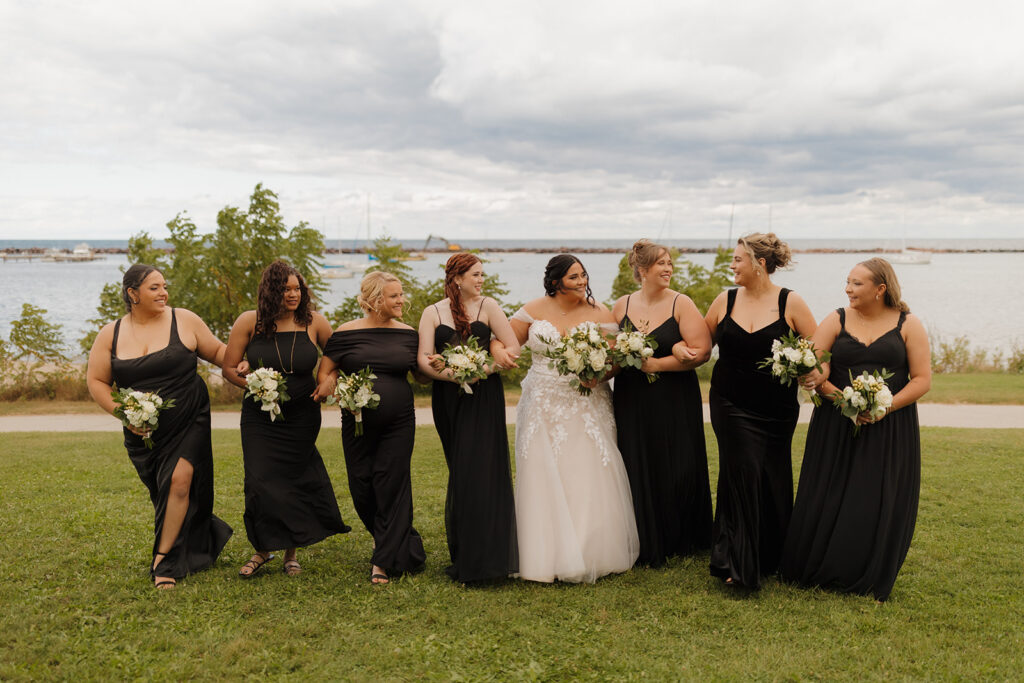 Bride walking arm-in-arm with bridesmaids in black dresses near Milwaukee's lakefront.