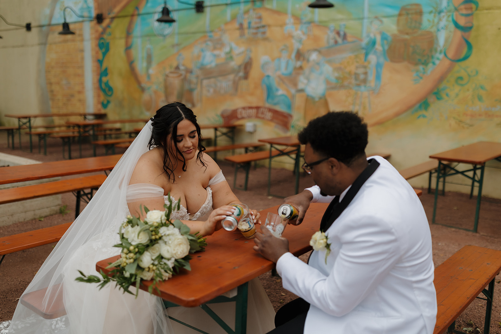 Couple pours beers together at a colorful outdoor beer garden during their Milwaukee wedding.