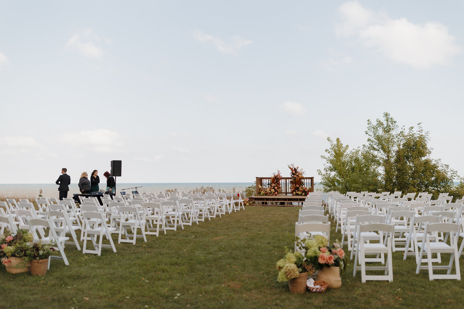 Wide view of a lakeside ceremony setup with white chairs, floral arrangements, and an altar stage, ready for a Wisconsin wedding celebration.