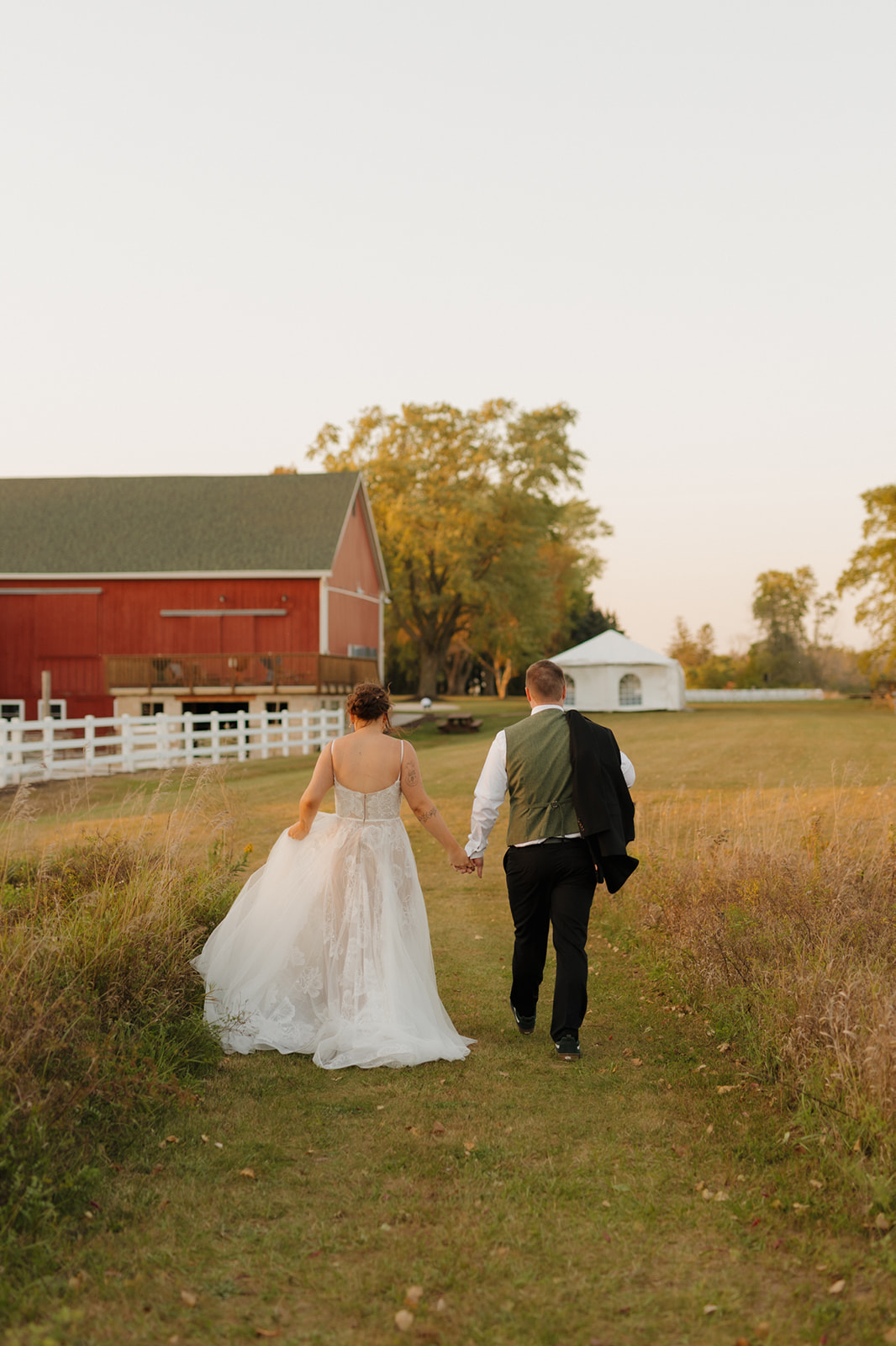 Bride and groom walking back towards red barn for wedding reception