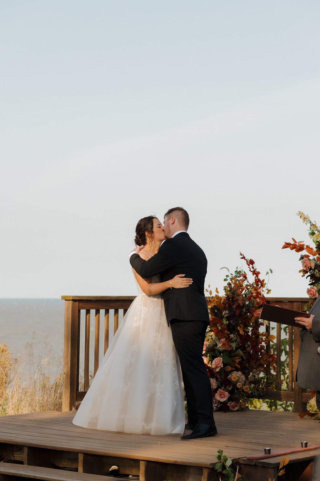 Bride and groom share their first kiss at a lakeside altar adorned with autumn florals during a heartfelt Wisconsin wedding ceremony.