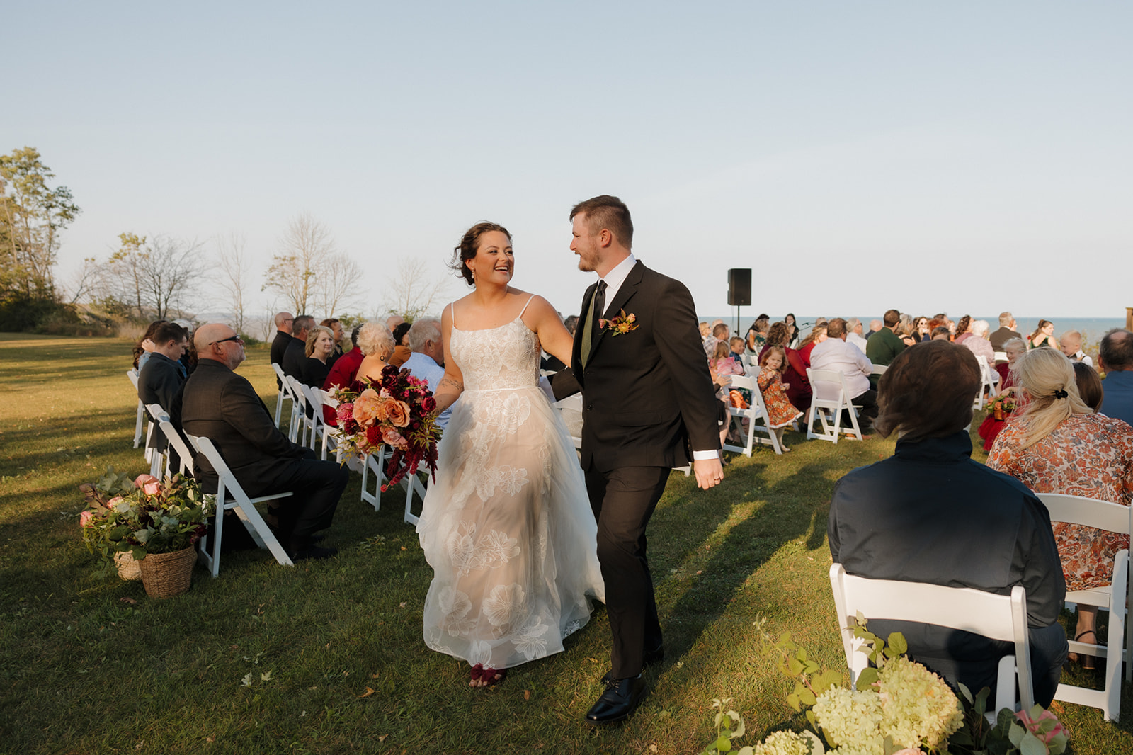 Just married! Bride and groom walk back down the aisle grinning, with guests seated by the lake during a Wisconsin wedding ceremony.