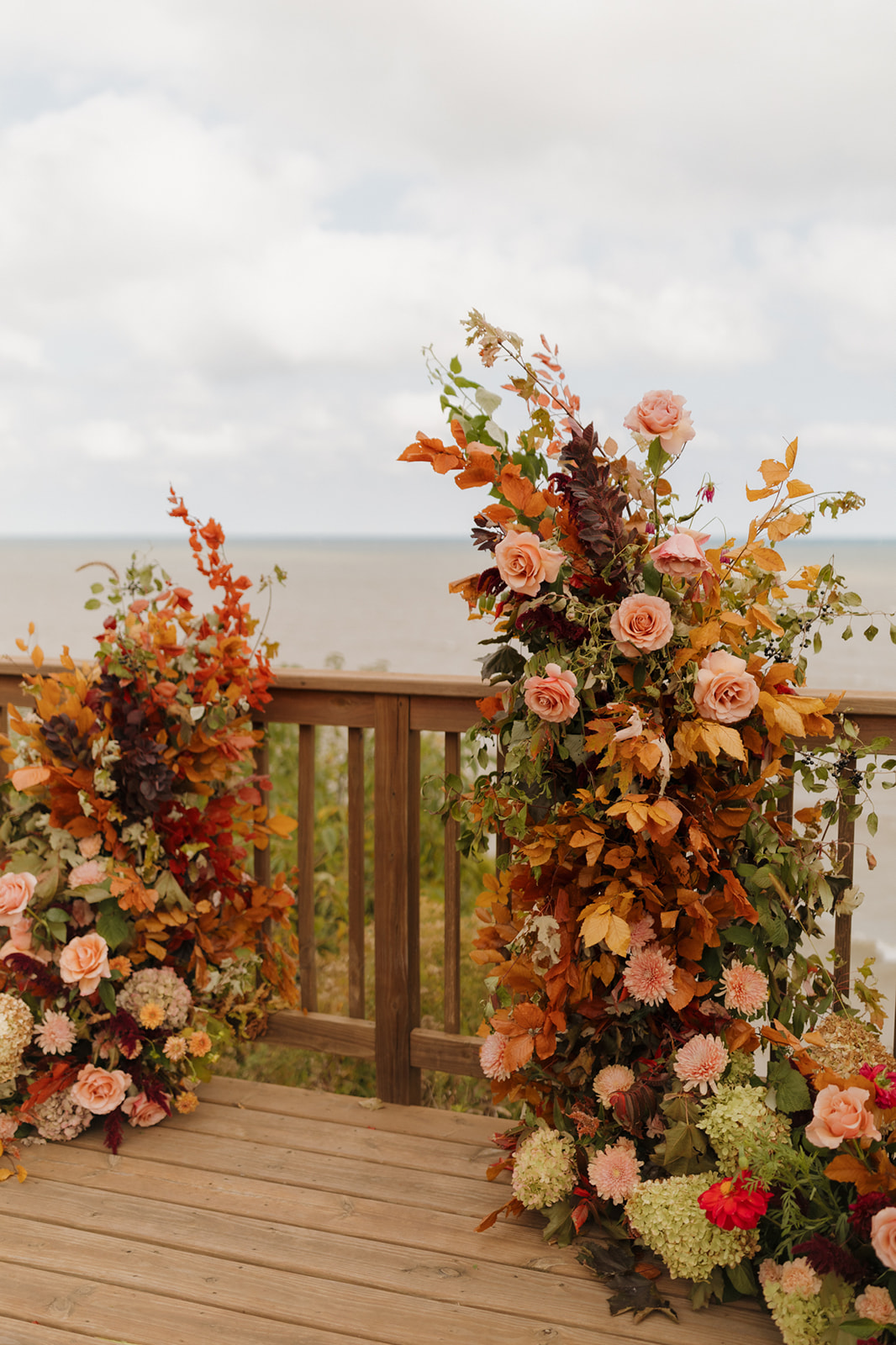 Lush autumn-inspired floral installation with roses, dahlias, and greenery on a lakeside deck for a Wisconsin wedding ceremony overlooking the water.