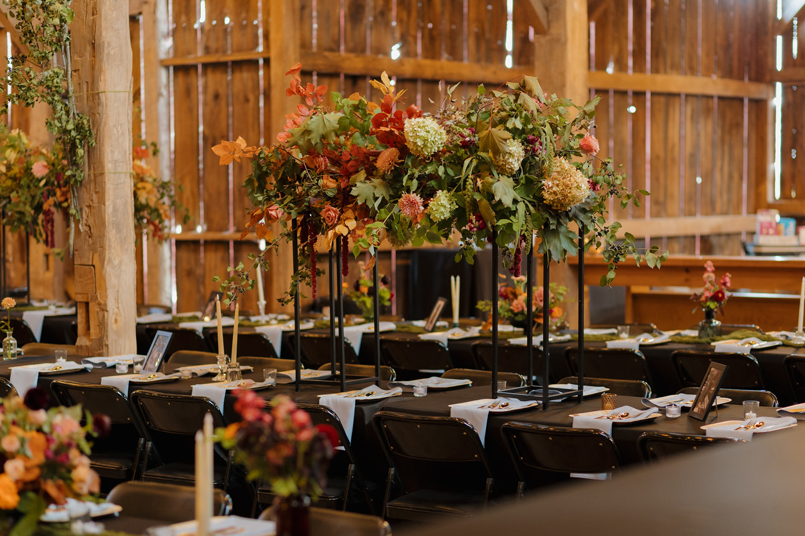 Rustic barn reception setup with dramatic fall floral centerpieces, black linens, and candlelit tables for an elegant Wisconsin wedding dinner.