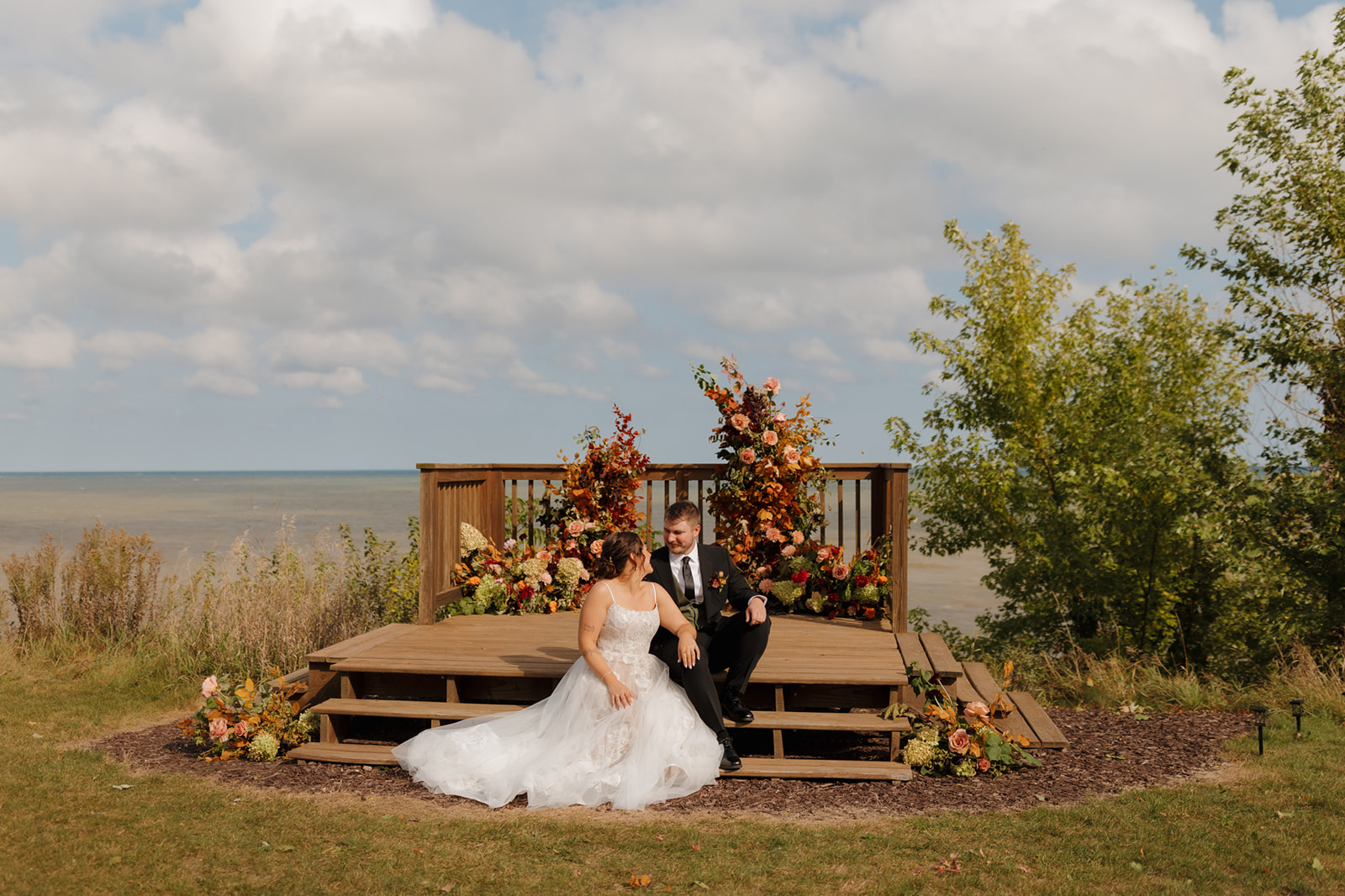 Bride and groom sitting on wooden dock beside lake after Wisconsin wedding weekend