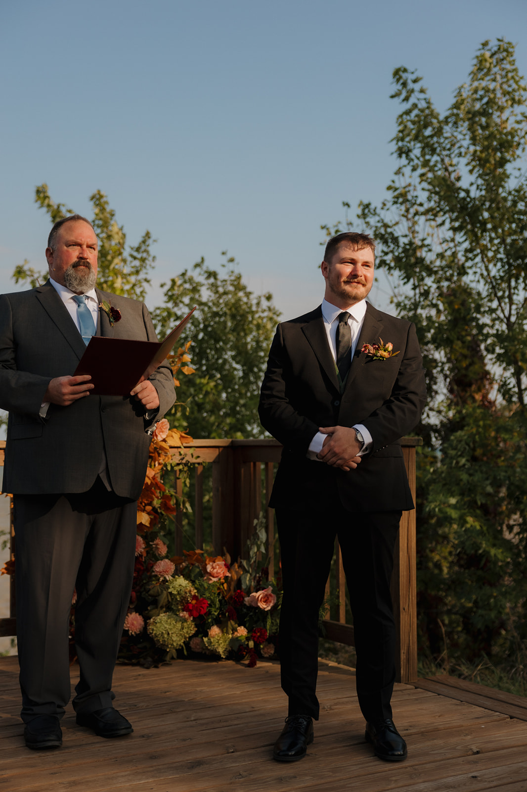 Groom smiling at the altar with floral decor and officiant by his side, eagerly waiting for his bride during their Wisconsin wedding ceremony.
