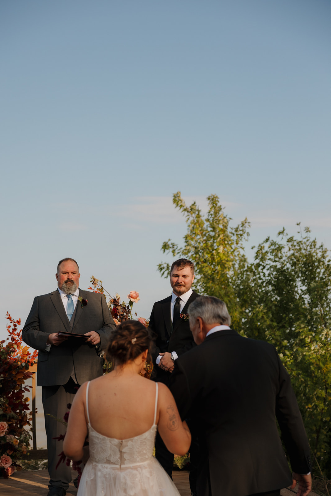 Bride approaches the altar arm-in-arm with her father, while the groom waits with emotion during their lakeside Wisconsin wedding ceremony.