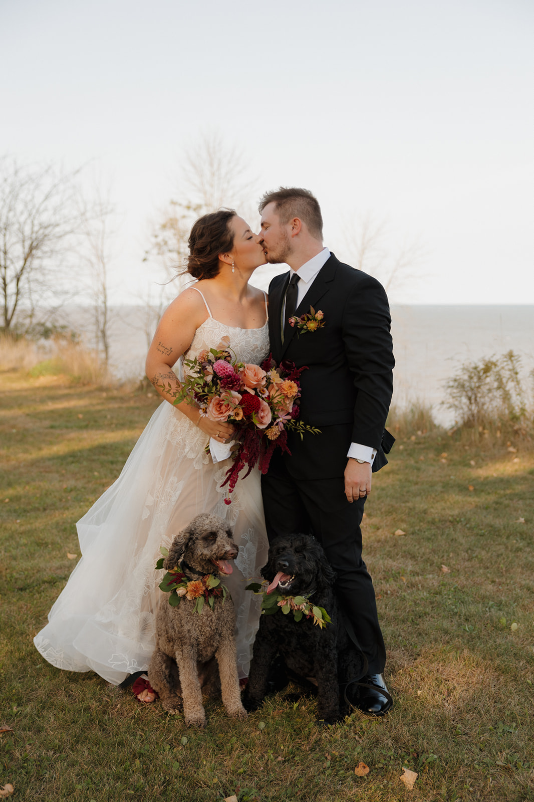 Bride and groom kissing with couple's pets in front of them wearing floral necklace