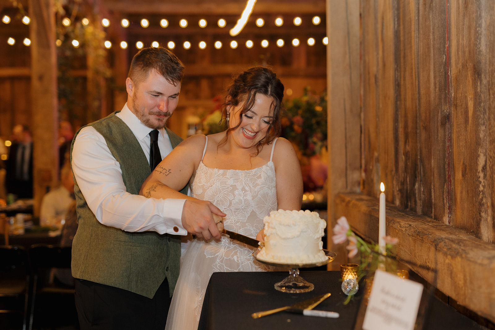 Couple cutting white traditional wedding cake during indoor wedding reception
