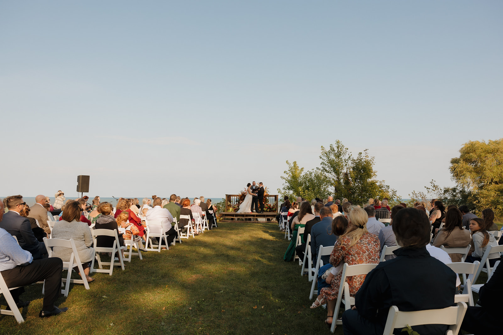 Guests seated in white chairs facing the altar during an outdoor Wisconsin wedding ceremony overlooking Lake Michigan.