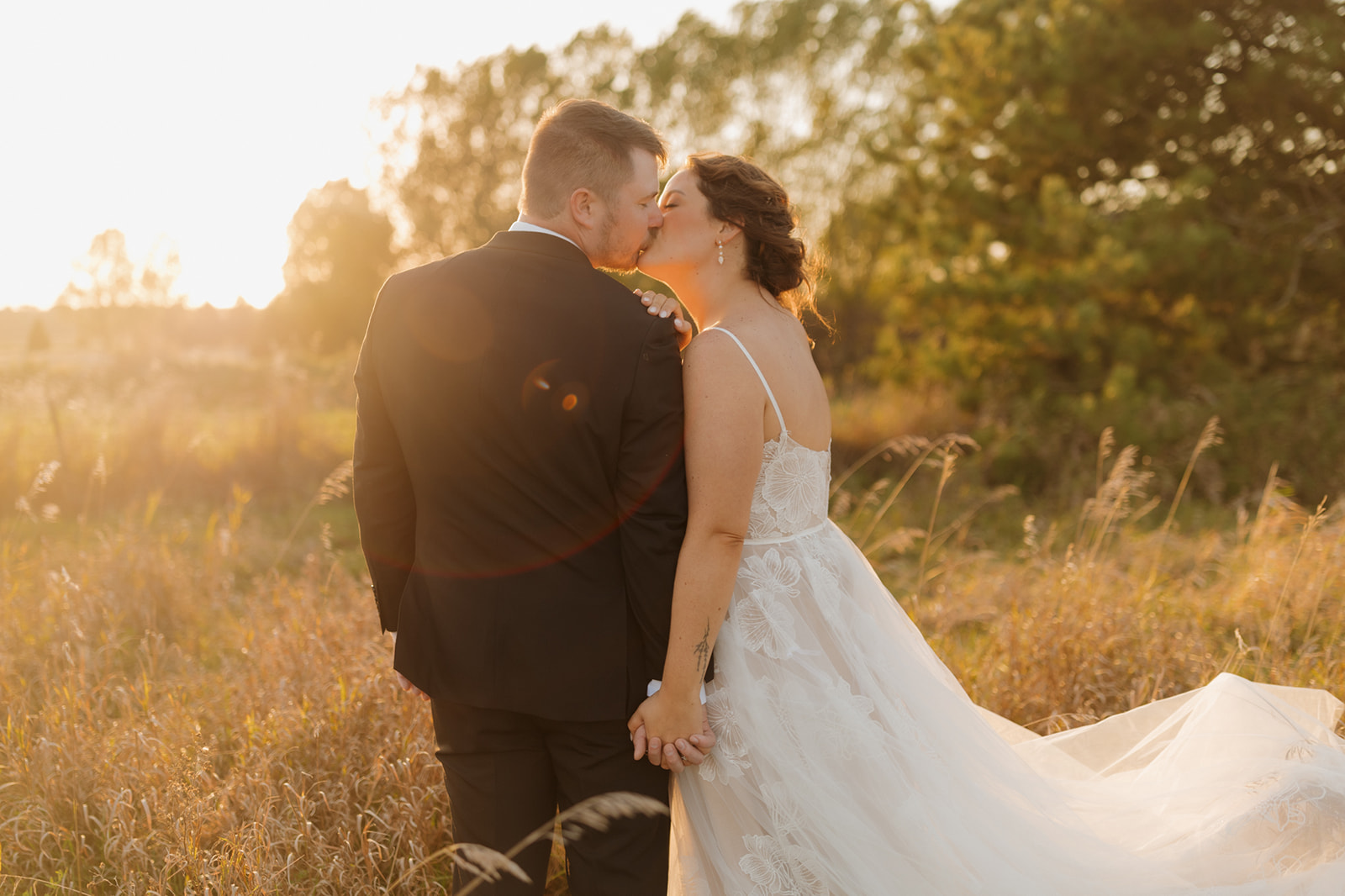 Bride and groom kiss in a golden field at sunset, surrounded by tall grasses and dreamy light during their Wisconsin wedding portrait session.
