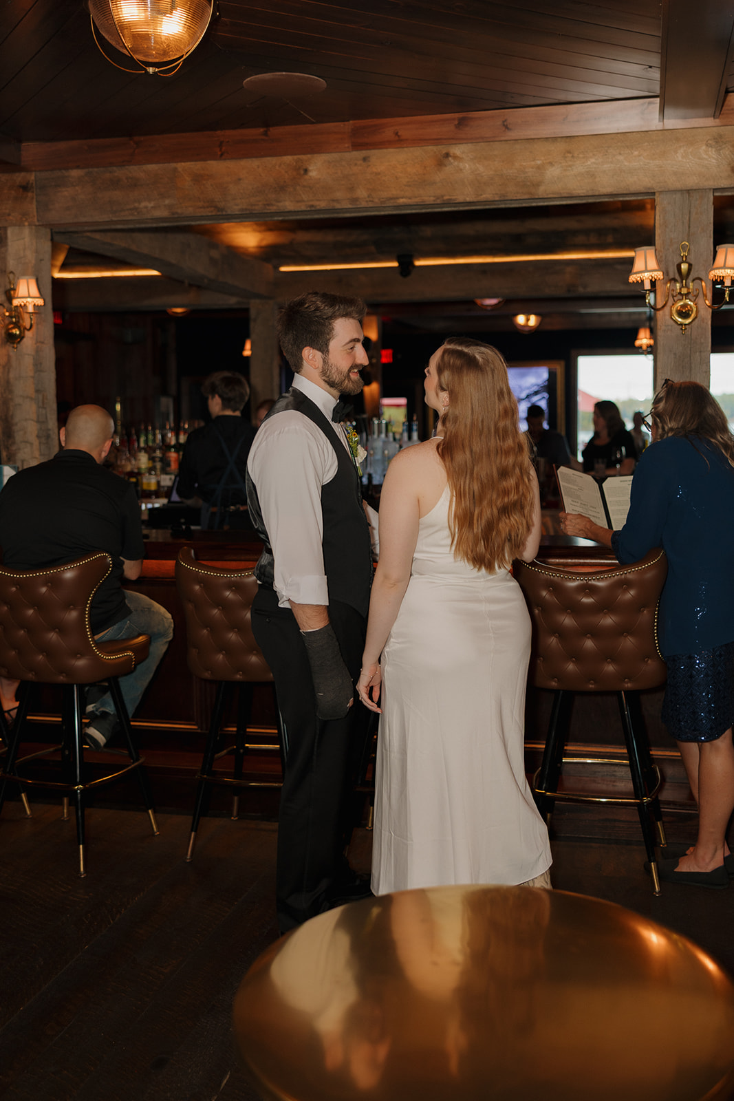 Couple sharing a quiet moment inside a rustic bar with leather stools and wood beams.
