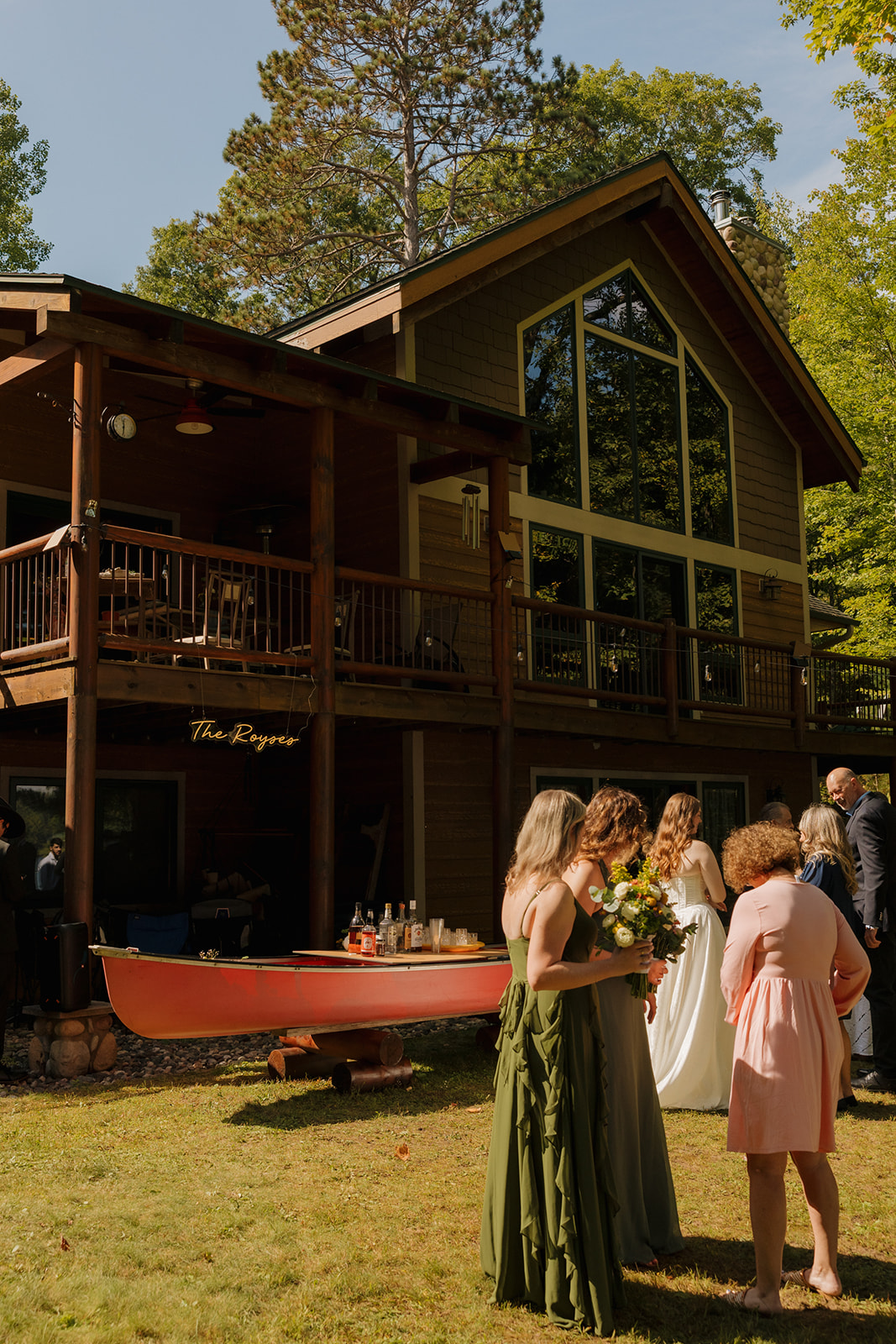 Guests mingling outside a log cabin as the bridal party prepares for the barn wedding reception.
