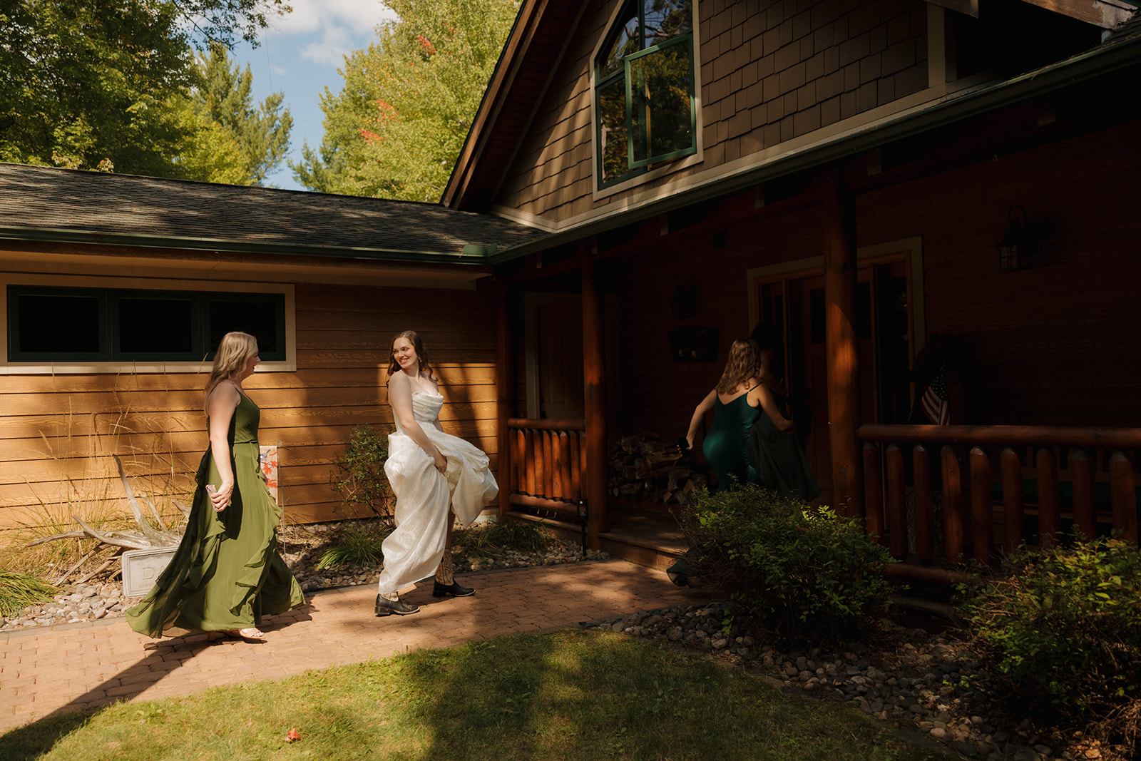 Bride walking with bridesmaids outside a rustic log-style home, smiling back over her shoulder.