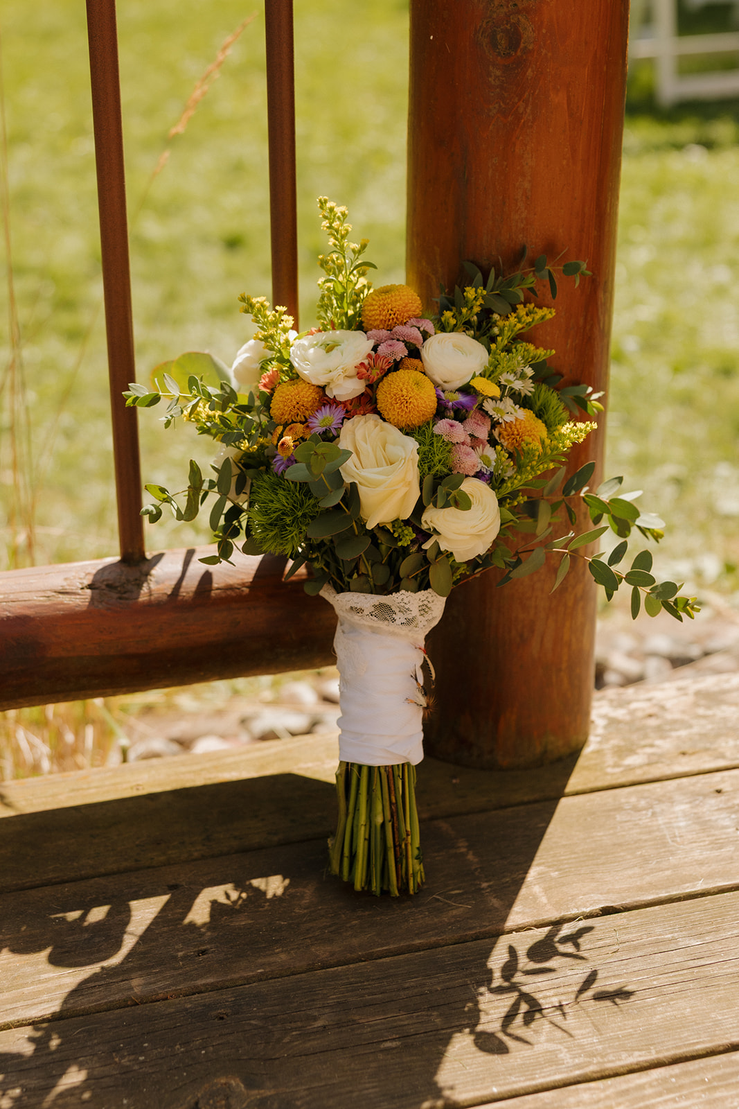Colorful bridal bouquet with yellow, white, and purple flowers resting on a wooden porch railing.