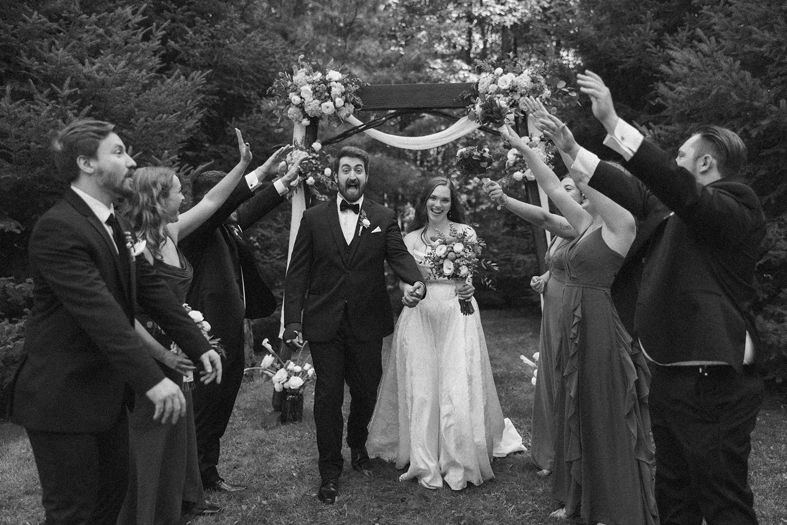 Bride and groom walking through a tunnel of cheering friends under the ceremony arch.