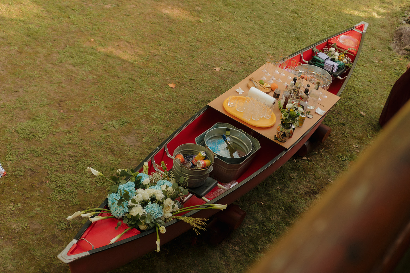 Canoe filled with drinks, flowers, and glasses repurposed as a creative barn wedding bar.