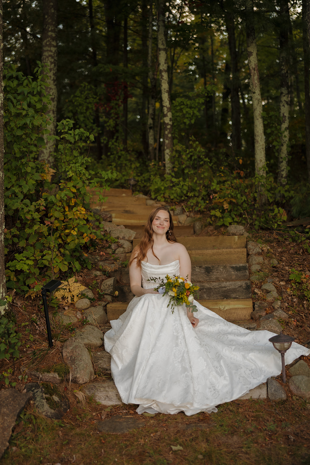 Bride sitting on stone steps in her wedding dress, holding her bouquet at a barn wedding.