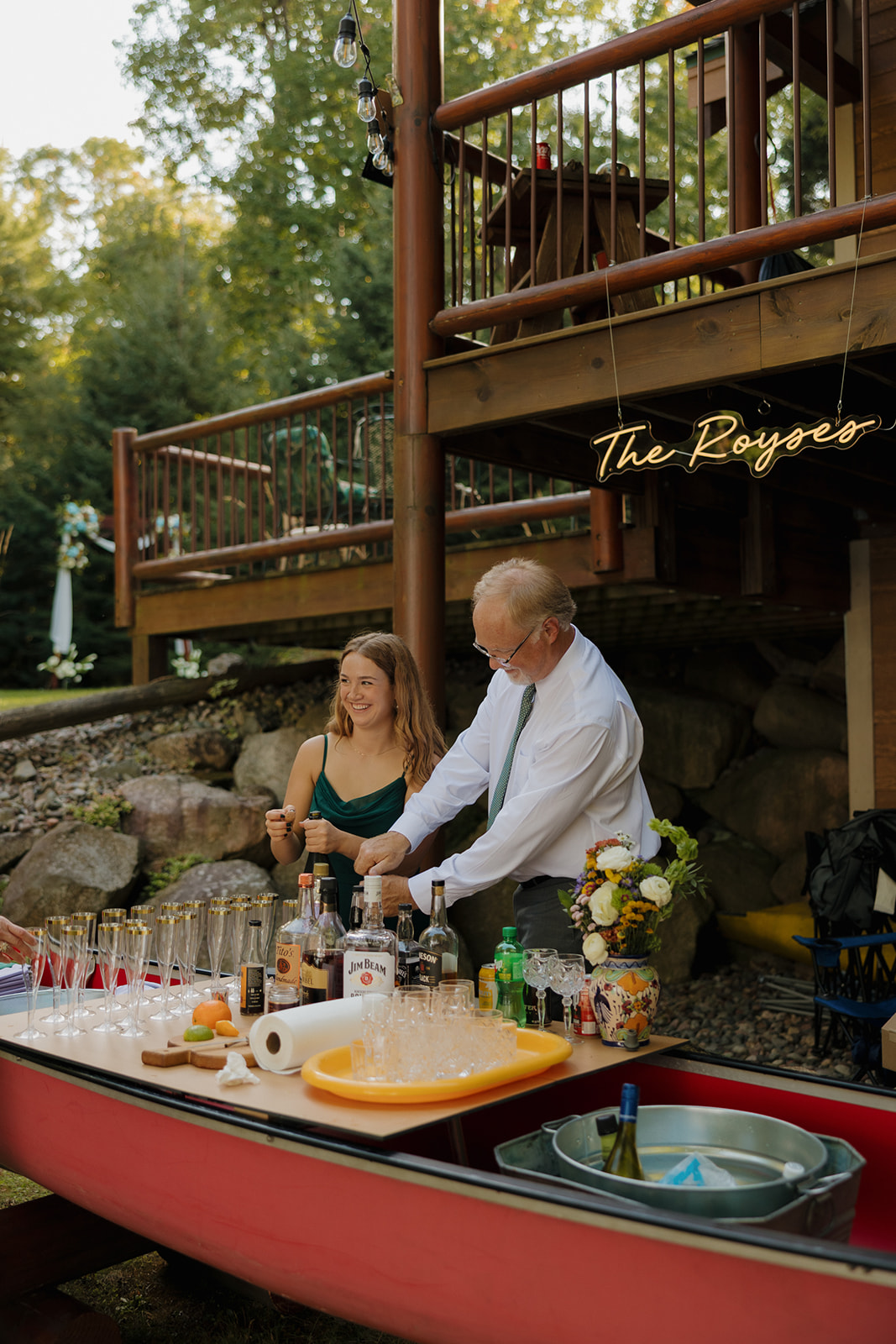 Father of the bride and bridesmaid serving drinks from a canoe bar at a barn wedding reception.