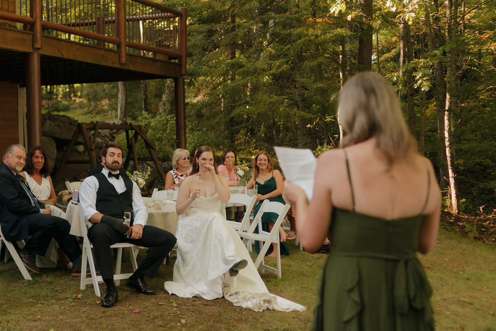 Wedding guests laugh as the maid of honor gives a toast during the outdoor reception.