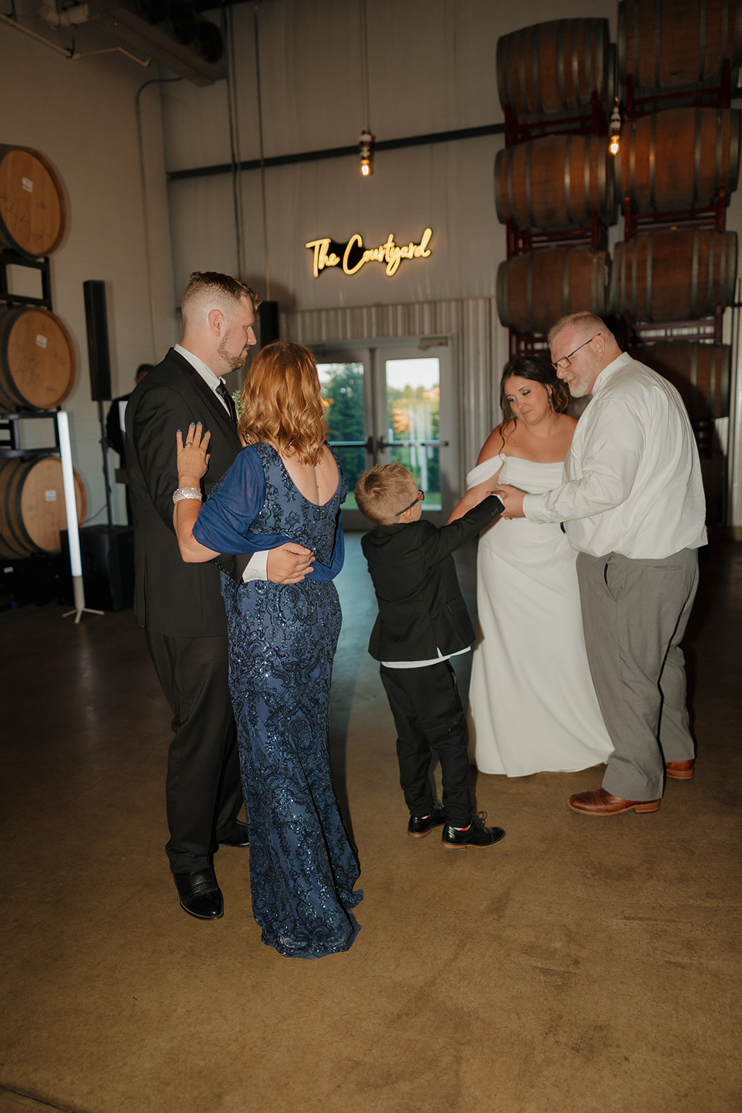 Bride and groom share emotional parent dances with their families on the dance floor surrounded by barrels at their Wisconsin brewery reception.