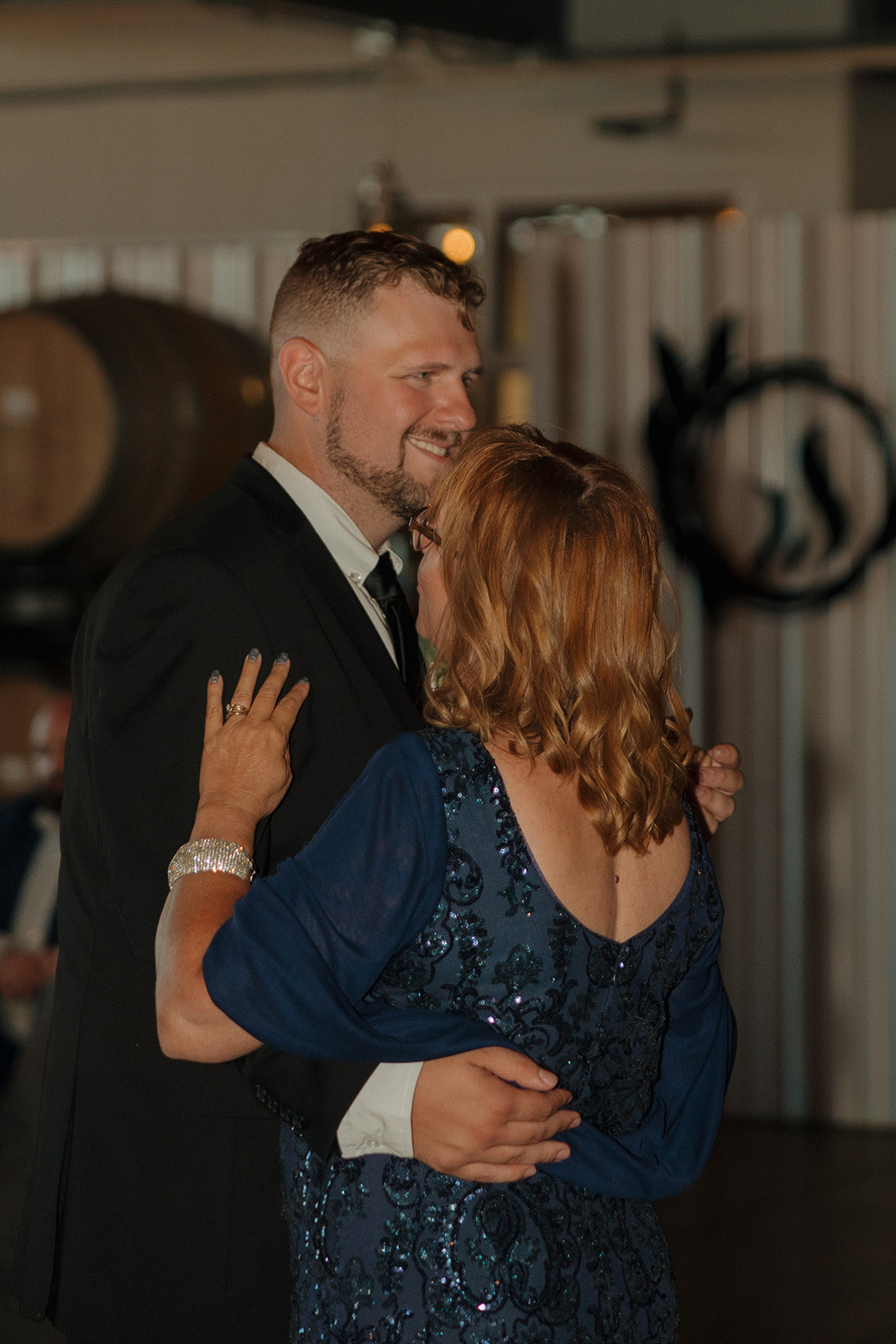 Groom smiles during a sweet mother-son dance moment inside the reception space at a Wisconsin brewery wedding.