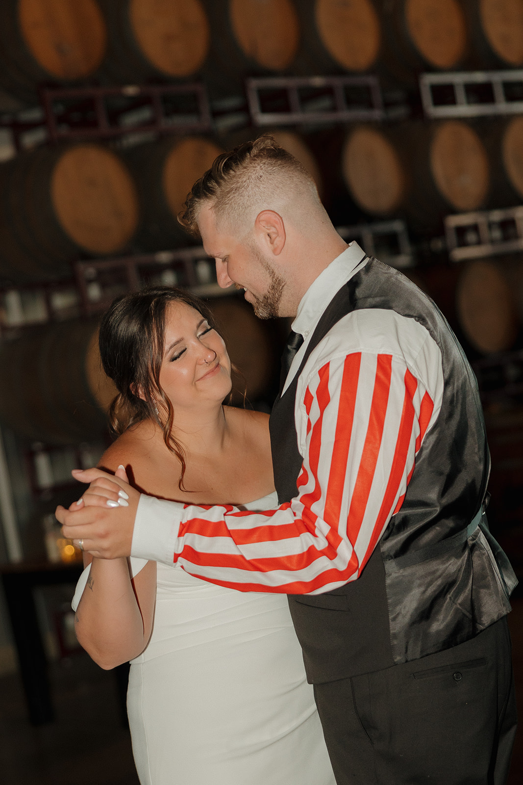 Bride and groom share their first dance surrounded by stacked brewery barrels, celebrating their Wisconsin brewery wedding.