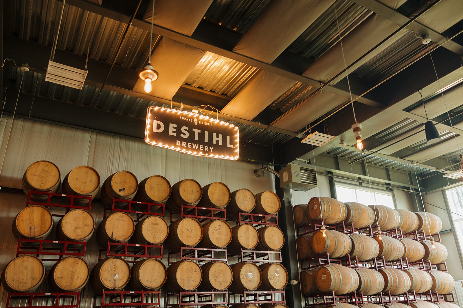 Stacked oak barrels and the glowing “DESTIHL Brewery” sign set the industrial-chic backdrop for a Wisconsin brewery wedding.